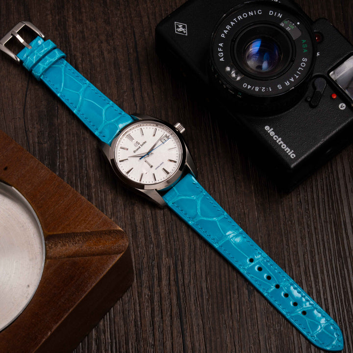 Grand Seiko Snowflake with blue strap and camera on a wooden surface